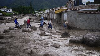 Personas vadean una carretera llena de barro tras el desbordamiento de un río provocado por las fuertes lluvias en El Castaño, Venezuela