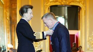 Princess Anne puting the order on its ribbon around Daniel Craig's neck 