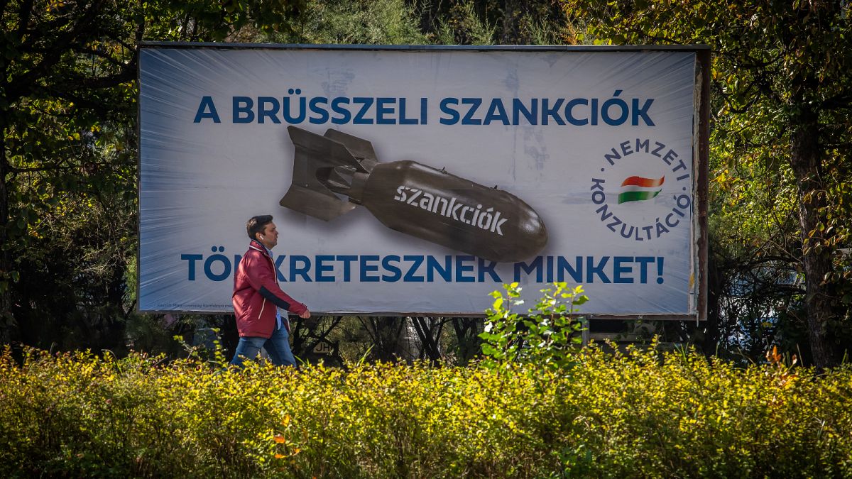 A man passes by a poster depicting a bomb reading "We are being punished by the Brussels sanctions", in Budapest on October 18, 2022