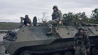 Ukrainian servicemen and a servicewoman, centre, pose for a photo with their armoured vehicle near Bakhmut, 22 October 2022