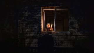 Catherine, 70, looks out the window while holding a candle for light inside her house during a power outage, in Borodyanka, Kyiv region