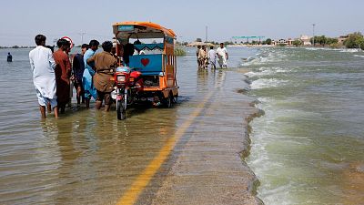Displaced people stand on flooded highway, following rains and floods during the monsoon season in Sehwan, Pakistan.
