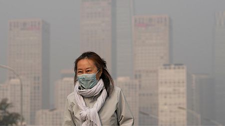 A woman wearing a face mask walks against the office buildings in Central Business District shrouded by pollution haze in Beijing.