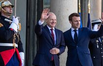 Olaf Scholz (balra) és Emmanuel Macron integet az Elysee-palota előtt