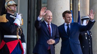 Olaf Scholz (balra) és Emmanuel Macron integet az Elysee-palota előtt