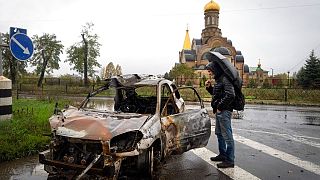 A passerby looks at a car damaged by Russian shelling in central Bakhmut, the site of the heaviest battle in the Donetsk region, Ukraine, Wednesday, Oct. 26, 2022.