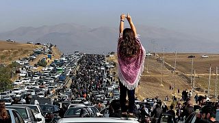 This image posted on Twitter shows an unveiled woman standing on top of a vehicle as thousands make their way towards Aichi cemetery in Saqez.