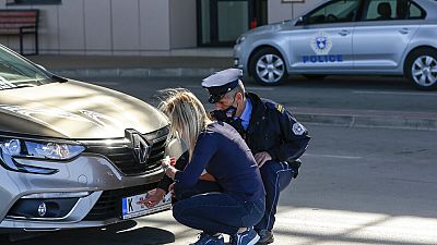 Un agente de policía de Kósovo ayuda a una conductora serbia a colocar pegatinas en la matrícula de su coche en un paso fronterizo.