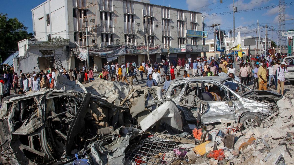 People walk amidst destruction at the scene, a day after a double car bomb attack at a busy junction in Mogadishu, Somalia Sunday, Oct. 30, 2022.