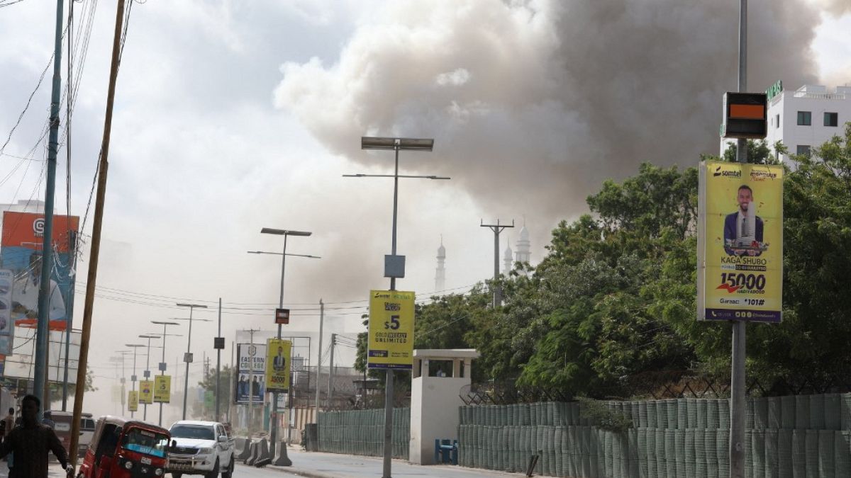Uma coluna de fumo eleva-se sobre a cidade enquanto as pessoas descem uma rua após uma grande explosão perto do Ministério da Educação, em Mogadíscio, a 29 de outubro de 2022