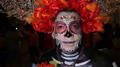 Revellers disguised as a Mexican Catrina poses for a picture