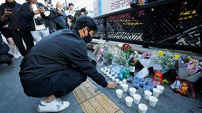 A man offers cups of wine to pay tribute for victims near the scene of a deadly accident in Seoul, South Korea, Sunday, Oct. 30, 2022, after Saturday's Halloween festivities.