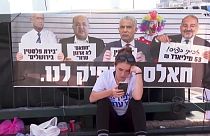 Una joven mira su teléfono m´óvil sentada frente a un cartel de la oposición a Netanyahu