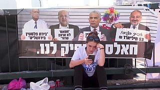 Una joven mira su teléfono m´óvil sentada frente a un cartel de la oposición a Netanyahu
