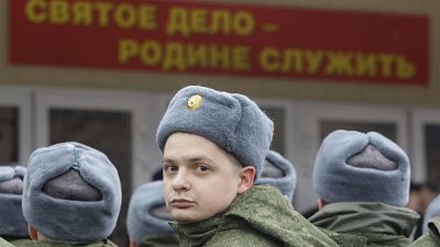 Russian military conscripts line up under a sign saying "Serving your motherland is a holy duty"