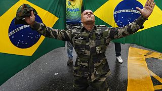 A supporter of President Jair Bolsonaro dressed in fatigues, kneels with his arms spread out in front of Brazilian national flags