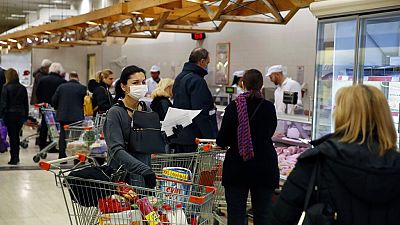A woman wearing a face mask holds a trolley as other customers wait in a queue to shop goods at a supermarket in Athens