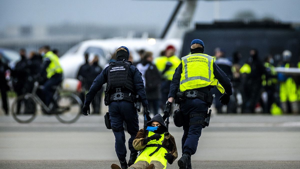 Sicherheitskräfte nehmen einen Klimaaktivisten am Flughafen Schiphol in Amsterdam fest.