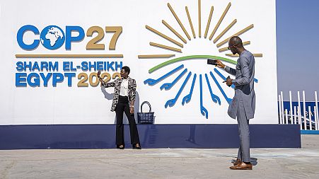 People pose for a photograph at the entrance of the COP27 UN Climate Summit, 6 November 2022