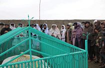 Taliban tarafından yayınlanan fotoğraflarda üst düzey isimlerin yeşil demir parmaklıklarla çevrili basit beyaz bir mezar etrafında toplandığı görülüyor