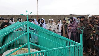 Taliban tarafından yayınlanan fotoğraflarda üst düzey isimlerin yeşil demir parmaklıklarla çevrili basit beyaz bir mezar etrafında toplandığı görülüyor