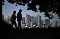 Walkers stroll in Greenwich Park with London's secondary central business district of Canary Wharf seen behind in the spring sunshine on May 6, 2022.