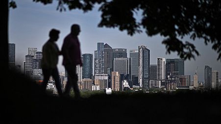 Walkers stroll in Greenwich Park with London's secondary central business district of Canary Wharf seen behind in the spring sunshine on May 6, 2022. 