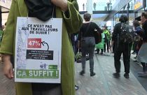 Woman with a sign saying "it is not for the workers to suffer" during protest in a Brussels shopping centre.