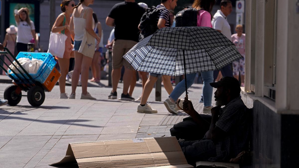 A man sits under an umbrella to shelter himself from the sun while begging for money in the street during hot weather in Madrid, Spain, Saturday, July 16, 2022.