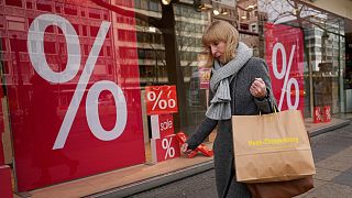 FILE - A woman walks with purchases past a store in Berlin, Friday, April 1, 2022. 