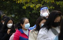 A worker wearing a face shield talks to people as they stand in line for COVID-19 tests at a coronavirus testing site in Beijing, Thursday, Nov. 10, 2022. 