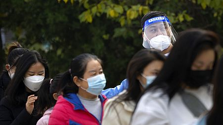 A worker wearing a face shield talks to people as they stand in line for COVID-19 tests at a coronavirus testing site in Beijing, Thursday, Nov. 10, 2022.