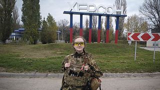 A Ukrainian female soldier poses for a photo against a Kherson sign in the background, in Kherson, 11 November 2022
