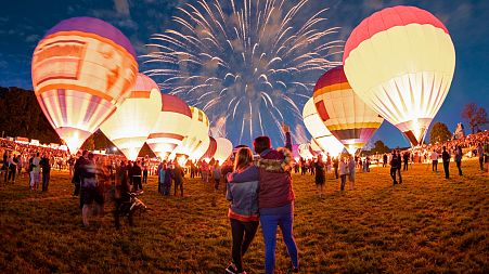 People watch fireworks and hot air balloons
