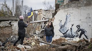 Frauen machen ein Foto vor einem Banksys-Kunstwerk an einem zerstörten Gebäude in Borodyanka