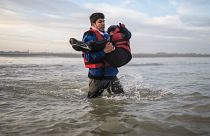 مهاجر يحمل طفلًا وهو يركض للصعود على متن قارب للمهربين على شاطئ قرب دنكيرك شمال فرنسا. 2022/11/12