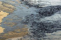 A person looks at oil sludge on a beach in Finisterre in Galicia, 1 December 2003