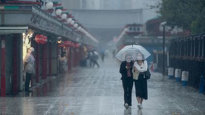 Two women wearing face masks share an umbrella as they walk on the main approach to the famed Sensoji temple in Tokyo.