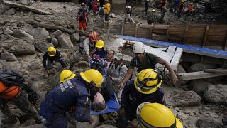 Trabajadores de emergencia llevan a una mujer rescatada de una zona inundada por un río que se desbordó. El 18 de octubre de 2022.
