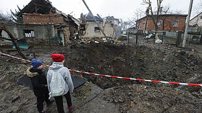 Παιδία κοιτούν ένα βαθύ λάκκο μετά από βομβαρδισμό στην Ουκρανία