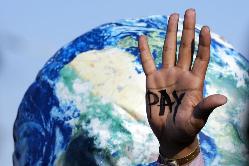 A hand reads "pay" calling for reparations for loss and damage at COP27 in 2022.