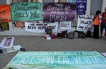 A climate activist sits near banners laid on the ground demanding protection of human rights, climate reparations, and countries' adherence to limit global temperature rise to