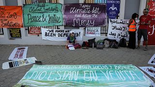 A climate activist sits near banners laid on the ground demanding protection of human rights, climate reparations, and countries' adherence to limit global temperature rise to