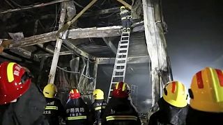 Rescuers use a ladder to climb into the remains of a fire at an industrial wholesaler in Anyang in central China's Henan province, 21 November 2022
