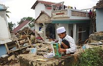 Uma criança apanha livros e manuais escolares nos escombros de uma escola destruída pelo sismo na Indonésia