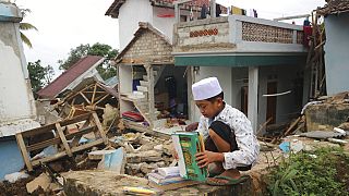 Uma criança apanha livros e manuais escolares nos escombros de uma escola destruída pelo sismo na Indonésia