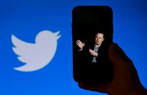 In this file photo taken on October 4, 2022, a phone screen displays a photo of Elon Musk with the Twitter logo shown in the background, 