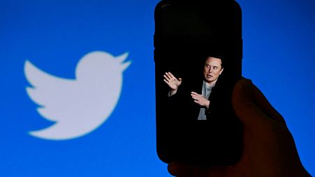In this file photo taken on October 4, 2022, a phone screen displays a photo of Elon Musk with the Twitter logo shown in the background,