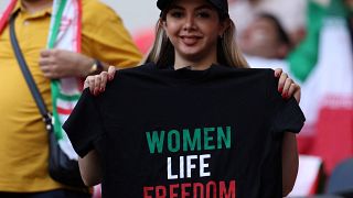 مشجعة إيرانية في قطر تحمل قميصا كتب عليه شعار الداعمين للاحتجاجات (نساء/حياة/حرية)