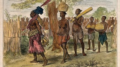 A Mrua medicine man or shaman with his assistants, Central Africa. Coloured wood engraving after V.L. Cameron.